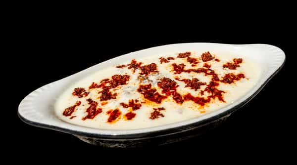 Oval dish of creamy white labneh or yogurt dip topped with seasoned ground meat and red oil.