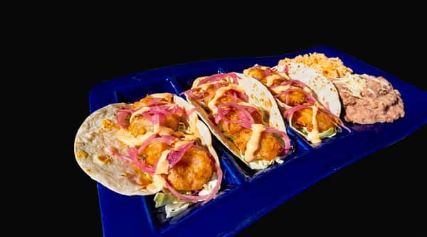 Three crispy fish tacos with pickled red onions and sauce, served with rice and refried beans on a blue tray.