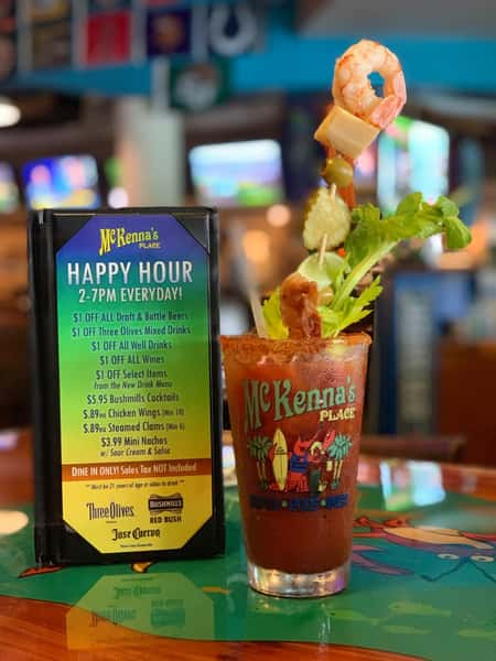 Bloody Mary cocktail at McKenna's Place topped with shrimp skewer, cheese cube, olives, celery, and crispy bacon, served during happy hour in a lively bar setting