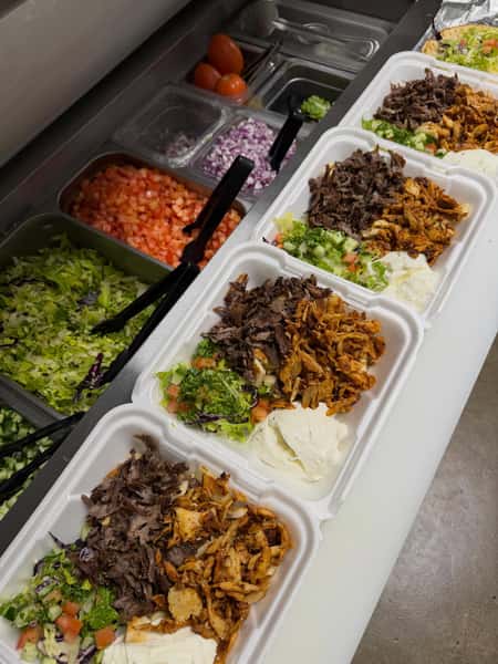 Turkish döner platters being assembled with beef and chicken, fresh Mediterranean salad, and creamy hummus at the prep station