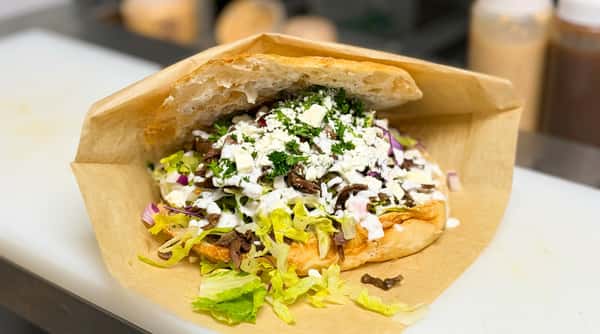 Open-faced pita sandwich with gyro meat, lettuce, red onion, white sauce, and crumbled feta cheese.