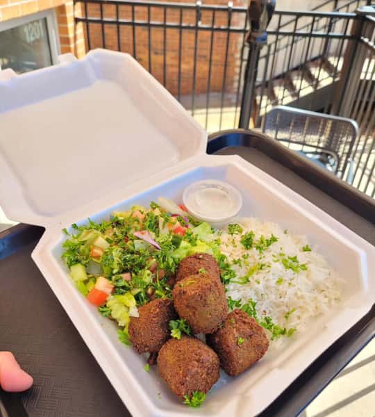 Falafel platter with crispy falafel, seasoned rice, fresh Mediterranean salad, and creamy garlic sauce served in a takeout container
