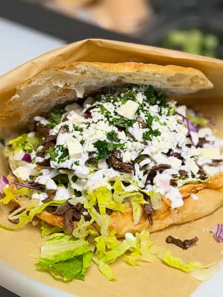 Loaded beef döner pita sandwich filled with fresh lettuce, red onions, feta cheese, herbs, and creamy garlic sauce