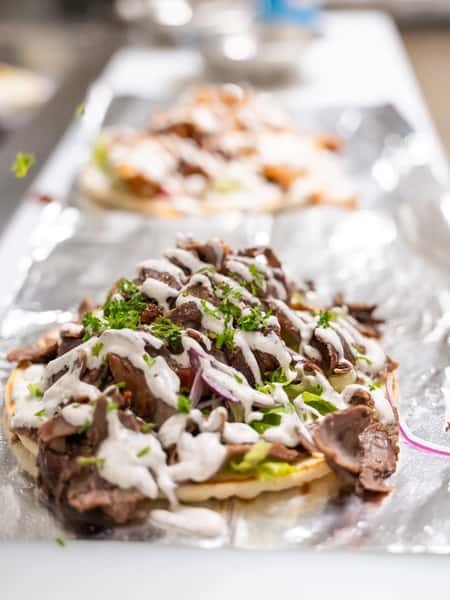 Fresh beef döner wrap being prepared with shaved meat, crisp vegetables, herbs, and creamy garlic sauce on warm flatbread
