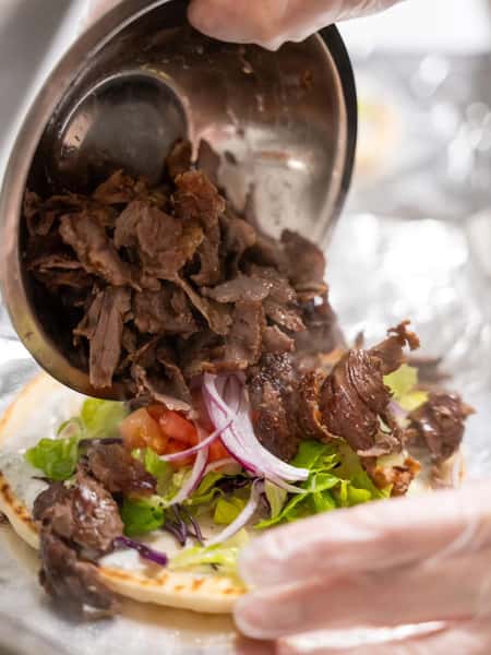 Authentic beef döner being layered onto warm flatbread with fresh lettuce, tomatoes, and red onions during wrap preparation