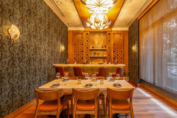 Intimate private dining room featuring a golden-hued bar with Persian lattice design, ambient lighting, patterned wallpaper, and an elegant dining setup for six.