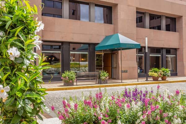 Charming exterior view of JOON restaurant with green canopy, blooming flowers, and large windows, offering a welcoming curb appeal in an urban setting.
