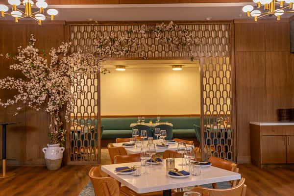 Elegant dining room in a Persian restaurant featuring warm wood tones, soft lighting, teal booth seating, and a decorative floral archway with patterned lattice dividers.