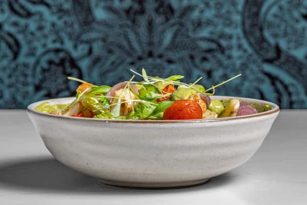 Colorful roasted vegetable salad featuring cherry tomatoes, cauliflower, pickled onions, and herb green dressing, topped with fresh microgreens in a rustic stoneware bowl.