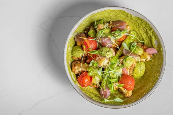 Top-down view of vibrant roasted cauliflower salad with cherry tomatoes, pickled onions, microgreens, and green herb dressing over creamy green purée.