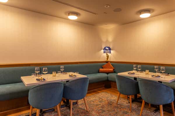 Warm and inviting dining corner with plush blue velvet chairs, modern white tables, soft lighting, and Persian-style accents for a relaxed yet upscale experience.
