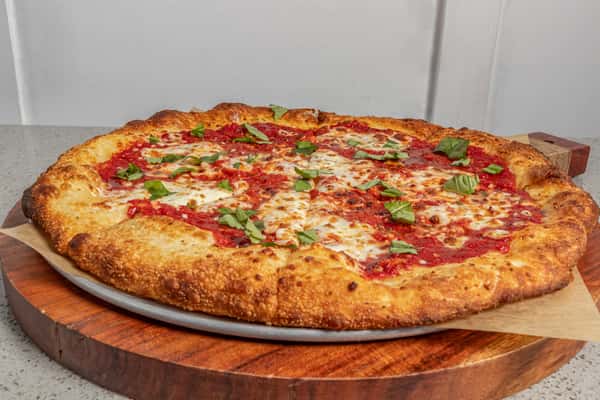 Classic Margherita pizza with fresh basil leaves, tomato sauce, and bubbly mozzarella on a crispy, golden crust.