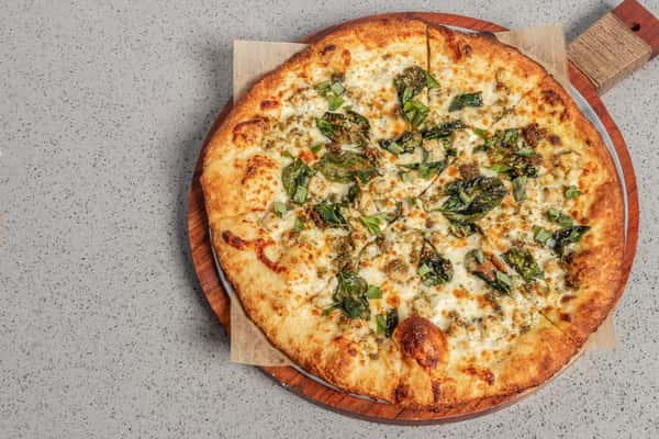 Pesto chicken pizza topped with grilled chicken, fresh basil, and rich pesto sauce over melted mozzarella, served on a golden crust and presented on a round wooden board.