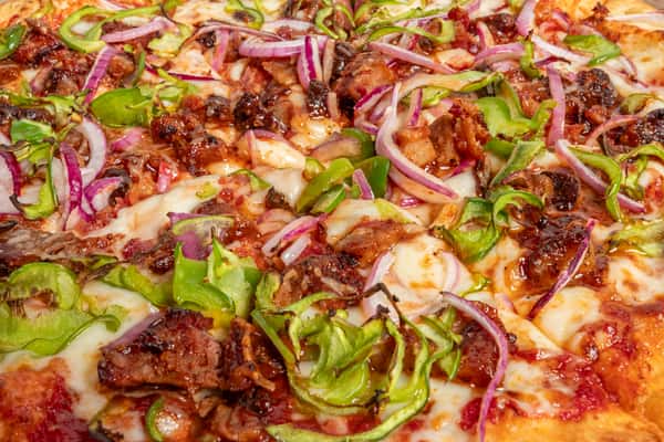 Close-up of a hearty meat pizza loaded with tender beef, green bell peppers, red onions, and melted mozzarella over tomato sauce.