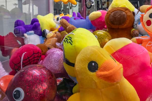 Colorful assortment of plush toys inside a claw machine, featuring ducks, bears, glittery balls, and cartoon characters at a family-friendly pizza shop.