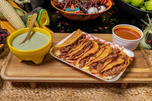 Golden birria tacos filled with juicy shredded beef and melted cheese, served on a checkered tray with a cup of rich consommé for dipping. Accompanied by creamy green salsa and traditional Mexican decor, showcasing an authentic and mouthwatering birria experience.