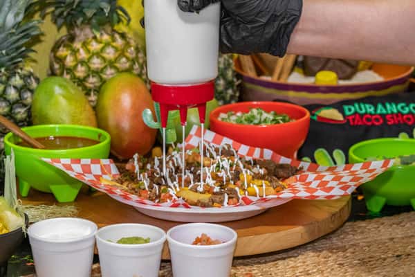 Loaded carne asada fries topped with grilled steak, diced tomatoes, cheese, and crema drizzle, being finished with a fresh topping of sour cream.