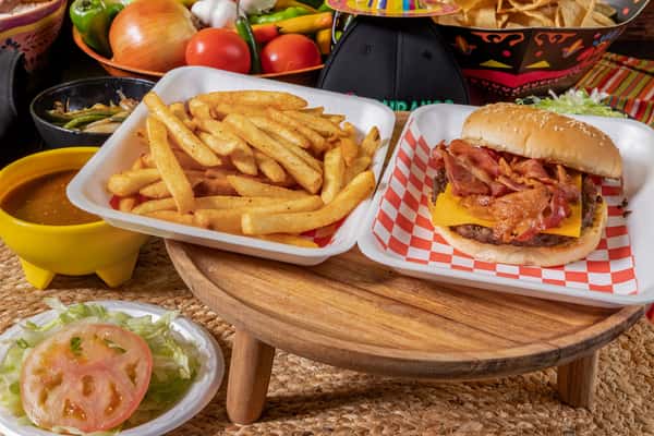 Classic bacon cheeseburger with a sesame seed bun, crispy bacon, and cheddar cheese, served alongside seasoned French fries and fresh vegetable toppings.