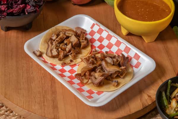 Pair of tacos de tripa (crispy beef intestine) served on soft corn tortillas, featuring golden-brown, savory pieces of meat. Presented on a red-checkered tray with a side of rich Mexican salsa, highlighting traditional street food flavors.