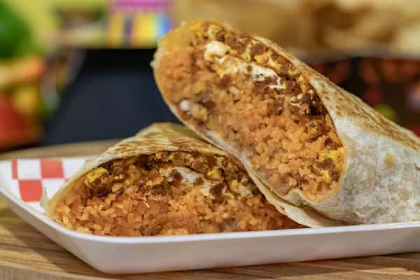 Mexican breakfast burrito filled with seasoned rice, scrambled eggs, and chorizo sausage, cut in half to reveal the hearty interior, served on a white tray with a checkered liner.