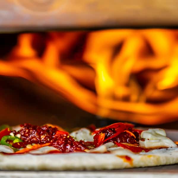 Pizza with red chili crisp, shredded peppers, and cheese baking in a fiery oven.