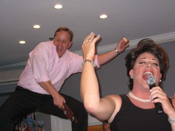 Energetic performance scene with a person singing into a microphone and another person behind them dancing with a bottle in hand.