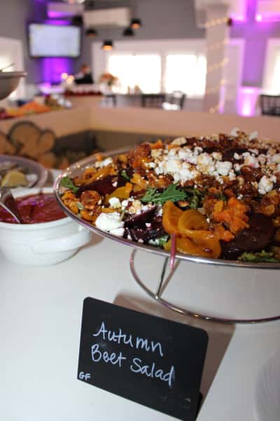 Colorful autumn beet salad with goat cheese, arugula, and roasted vegetables on a buffet table with a chalkboard label.