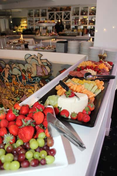 Colorful fruit and cheese charcuterie spread with strawberries, grapes, melon, and cheese cubes on a white buffet table.