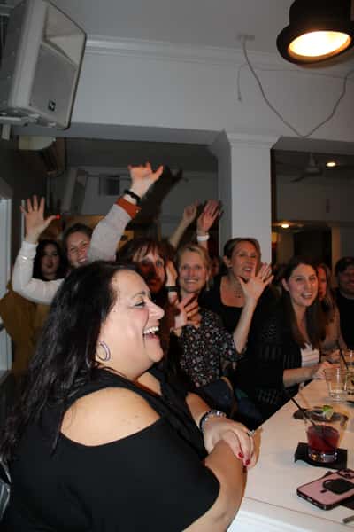 Women laughing and cheering at a bar, some with hands raised, enjoying drinks and conversation.