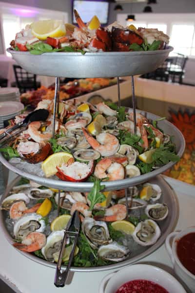 Tiered seafood tower filled with oysters, shrimp, clams, and lobster garnished with lemon wedges and greens.
