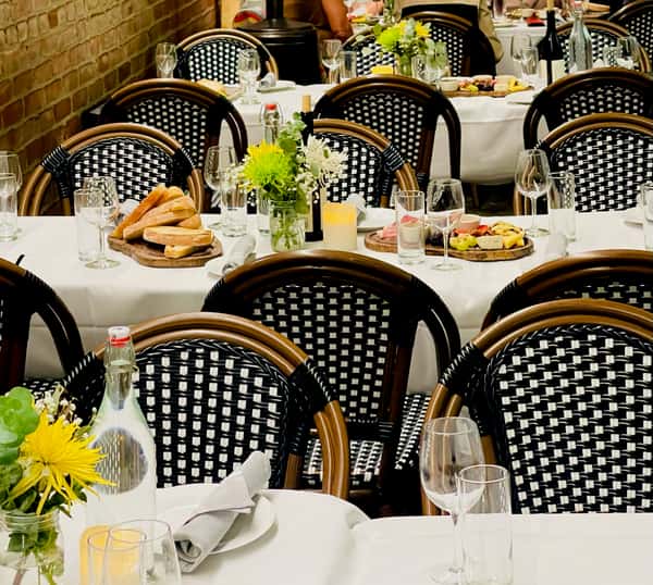 Charming outdoor dining area with wooden tables, elegant table settings, and vibrant flowers, nestled between brick walls, perfect for a cozy meal.