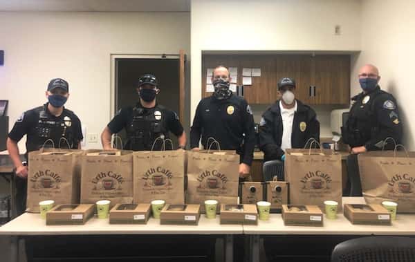 Five Laguna Beach police officers standing behind long table with brown Urth bags and lunch boxes
