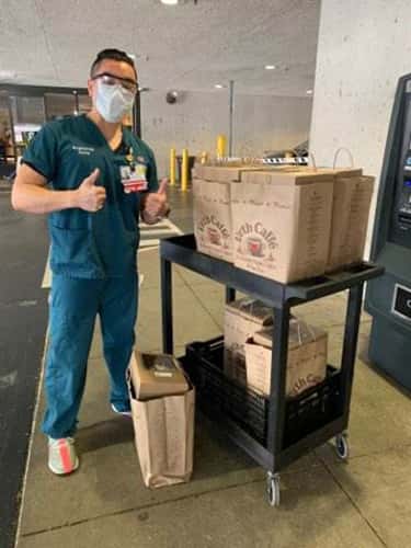 Male nurse with mask giving thumbs up standing next to a cart full of Urth food bags.