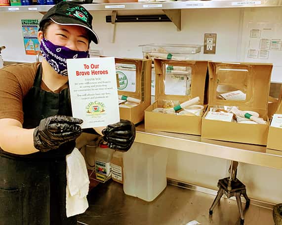 Urth Caffé employee with bandana mask holding To Our Brave Heroes card.