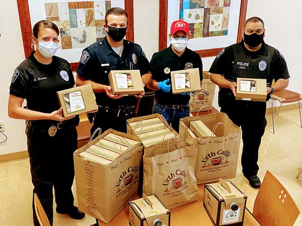 3 police and one Urth employee standing at table loaded with Urth Caffé lunch boxes