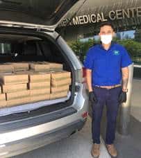 Back of mini-van packed with Urth Caffé lunch boxes with masked nurse getting ready to unload them.