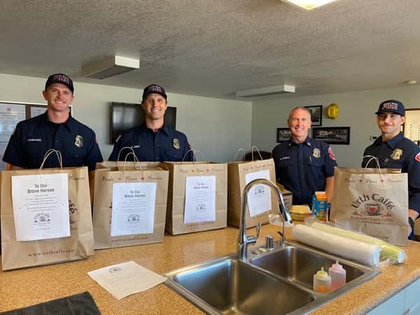 Laguna Beach firemen behind table with Urth food bags in front of them.