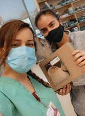 Two nurses upclose with masks, on is holding a lunch box from Urth Caffé.