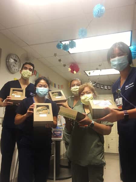 Group of five medical personel with masks in hallway all holding lunch boxes.