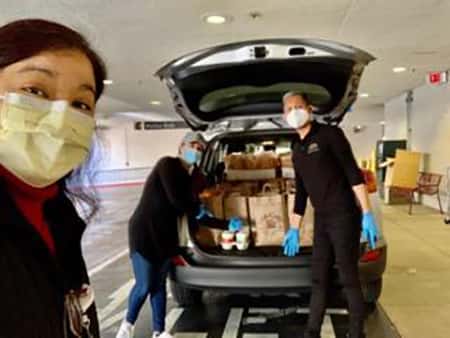 Three nurses unloading back of minivan full of Urth Caffé food bags and lunch boxes.