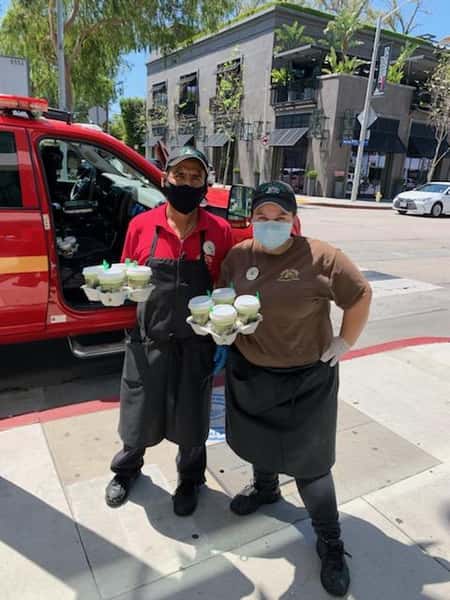 2 Urth Melrose employees holding drinks in from of parked emergency vehicle
