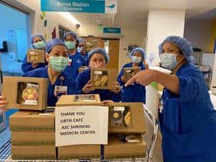 Six nurses in blue scrubs and masks next to a table full of Urth Caffé lunch boxes with Thank You sign.
