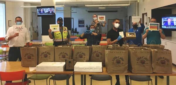 Group of Beverly Hills Public Works employees standing behind long table with many brown Urth bags of lunch boxes. The poeple are holding Thank You cards.