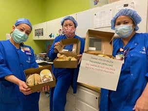 Three nurses in blue scrubs with masks holding open lunch boxes from Urth Caffé.