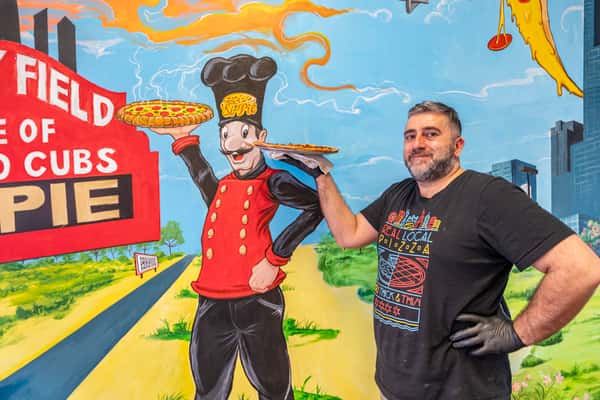 Chicago's Si-Pie Pizzeria owner, Simon Mikhail, standing alongside the iconic wall-art.
