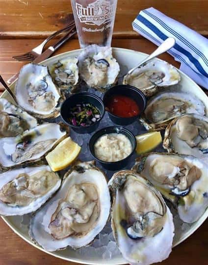 oysters on the half shell in a bucket full of ice with dipping sauces