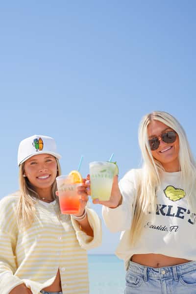 Friends raising colorful frozen cocktails under a clear blue sky at Sandbar, capturing the fun of waterfront dining.