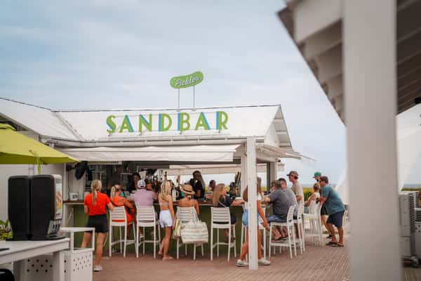 Guests dining and socializing under covered outdoor seating at a popular beachfront restaurant.