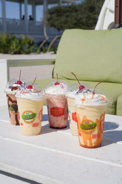 Colorful milkshakes topped with whipped cream, cherries, and sweet toppings at a family-friendly beachfront restaurant.
