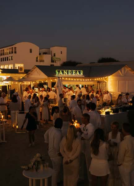 Crowd gathered for an evening event at a lively beachfront restaurant and outdoor bar.